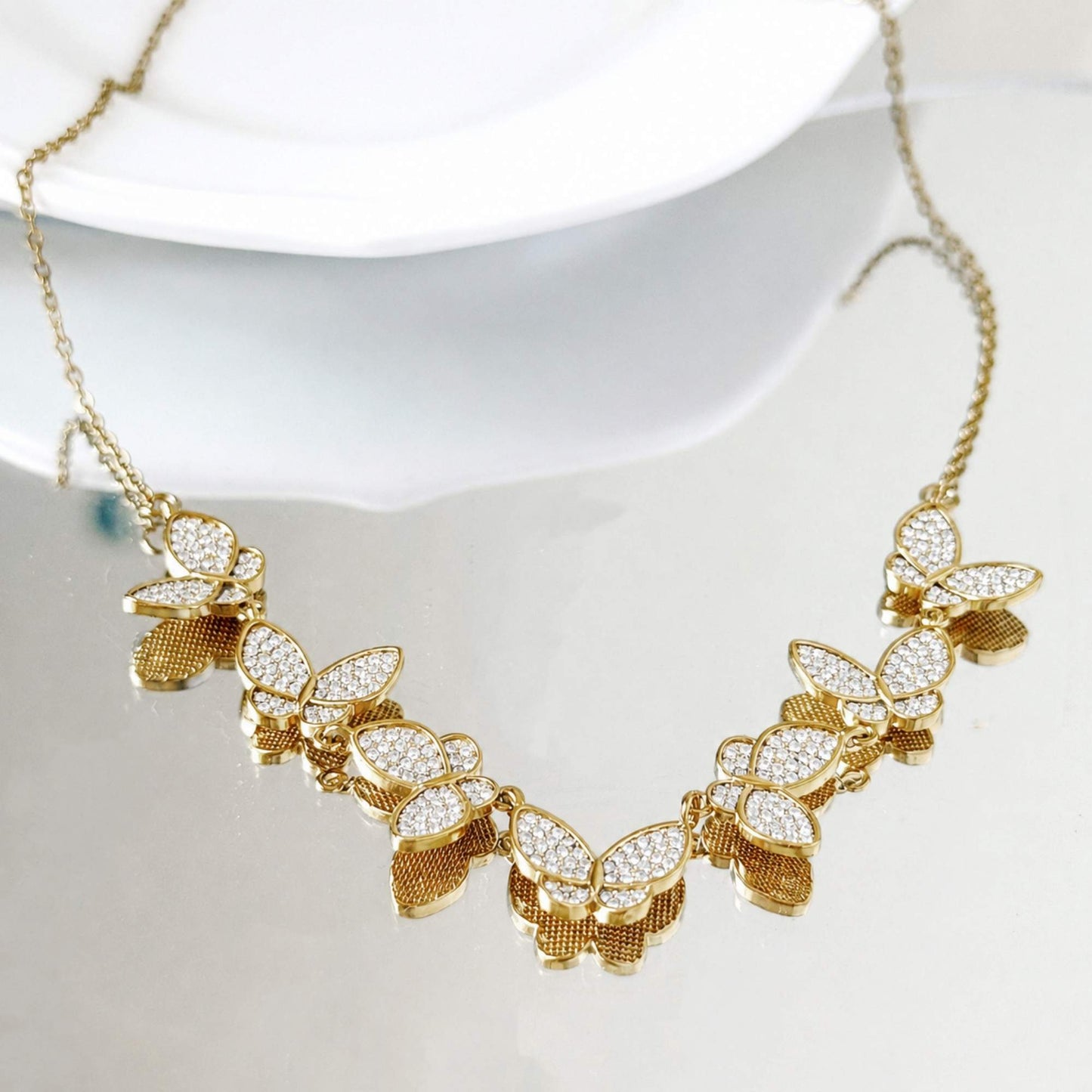 Gold butterfly zircon necklace arranged on a soft white plate in natural light.