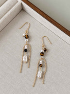 Tether natural tiger eye and pearl earrings arranged on a neutral linen jewelry tray.
