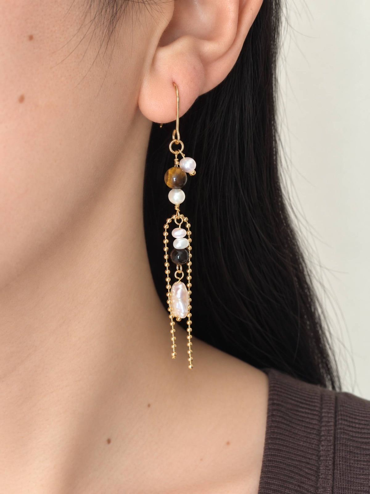 Tether tiger eye and freshwater pearl drop earring worn in side profile, showing its long open-frame silhouette.