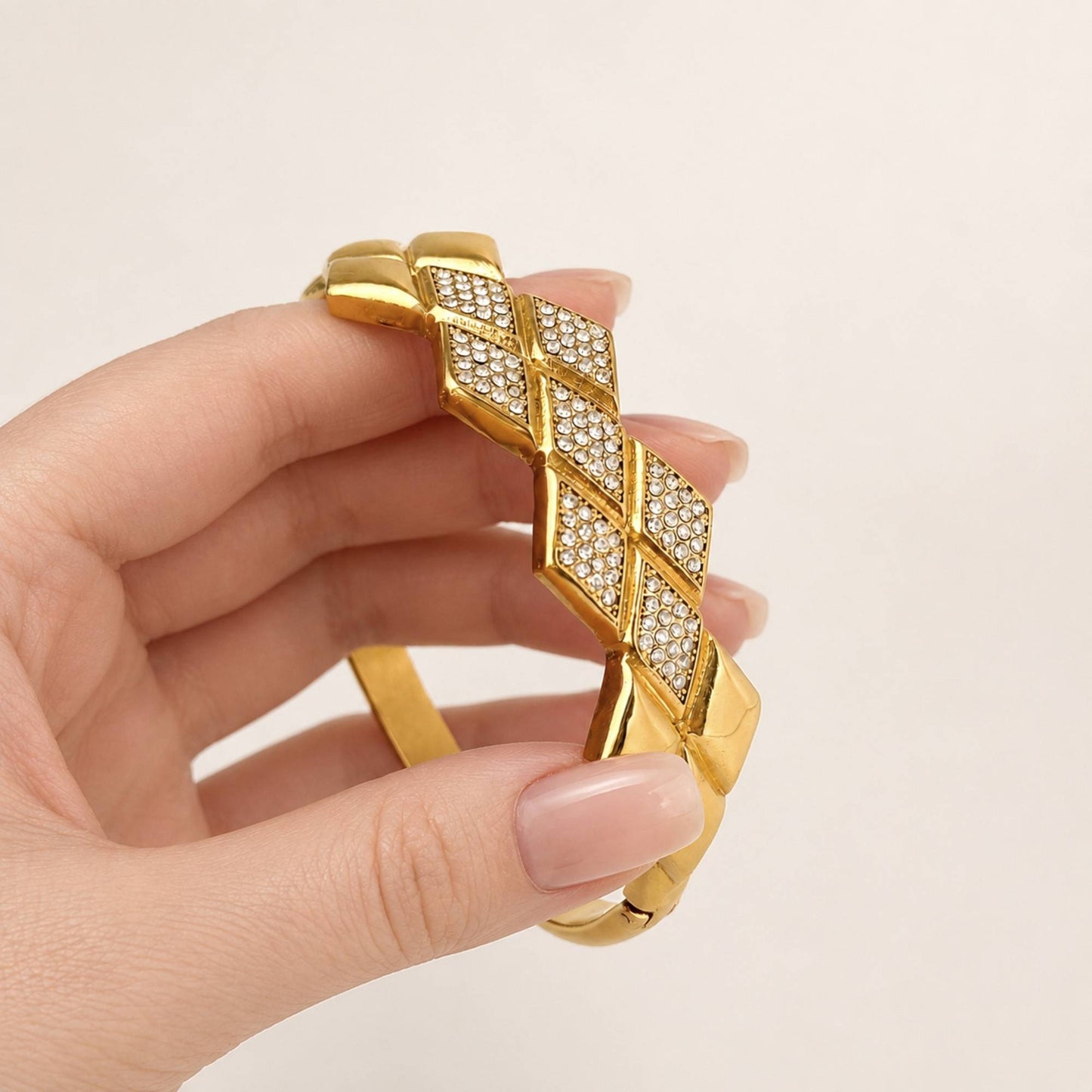 Close-up of the Woven CZ Bangle held by hand, showing the overlapping geometric panels and cubic zirconia details
